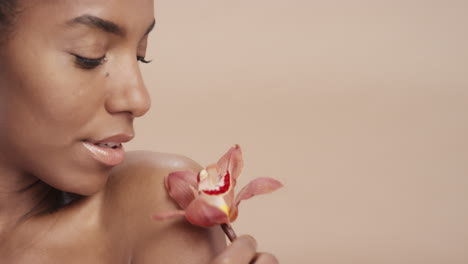 Cerrar-Retrato-De-Belleza-Atractiva-Mujer-Afroamericana-Tocando-El-Cuerpo-Con-Flor-De-Orquídea-Acariciando-Una-Tez-De-Piel-Sana-Disfrutando-De-Una-Suave-Fragancia-De-Esencia-Natural-Concepto-De-Cuidado-De-La-Piel