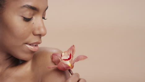 retrato de belleza de cerca mujer afroamericana atractiva tocando el cuerpo con una flor de orquídea acariciando una piel sana disfrutando de la suave fragancia de la esencia natural concepto de cuidado de la piel