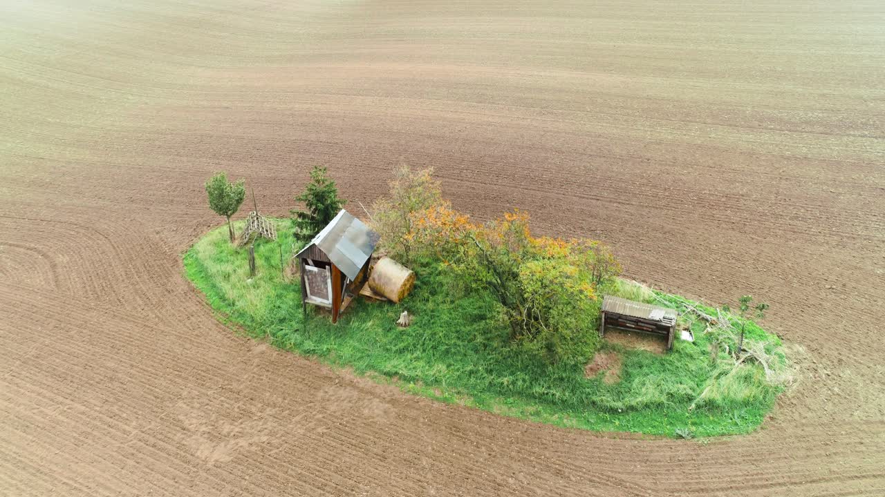 Plowed brown farmland with a green piece of land. Aerial forward