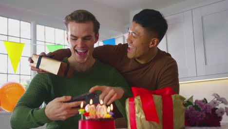 same sex male couple celebrating 30th birthday at home with  man taking photo of cake on phone