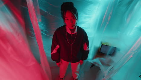 asian woman in retro tracksuit posing in dark studio with neon light