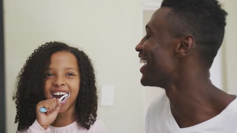 african american father and daughter brushing their teeth