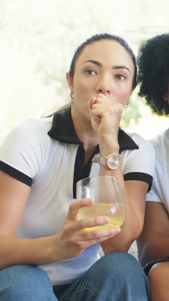 Vídeo vertical: Observando fora da tela, dupla no sofá, homem se afastando, mulher de polo segurando uma taça de vinho.