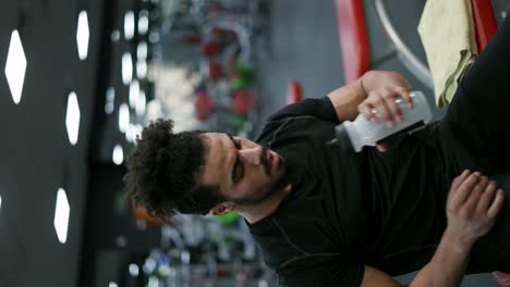 el hombre sentado y bebiendo agua después de terminar el curso de entrenamiento con pesas en el gimnasio
