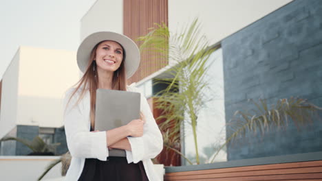 una mujer con una computadora portátil frente a una casa moderna.