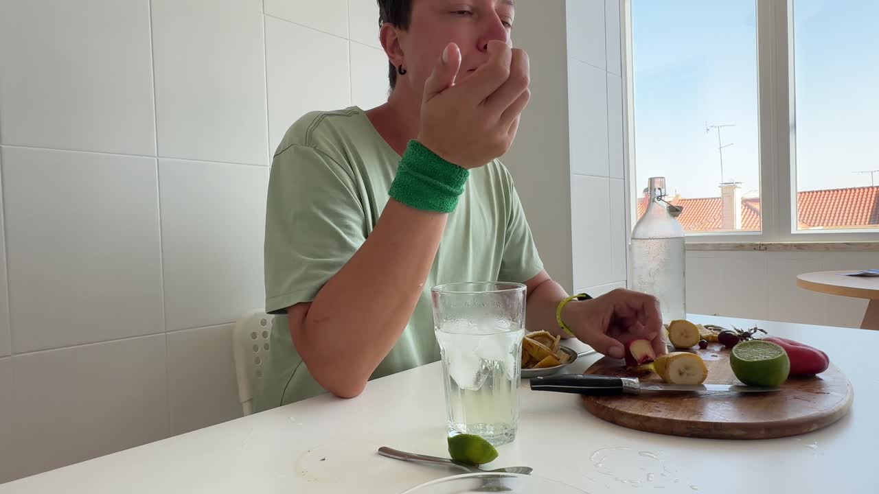 Giovane uomo che mangia e taglia frutta fresca in una cucina luminosa