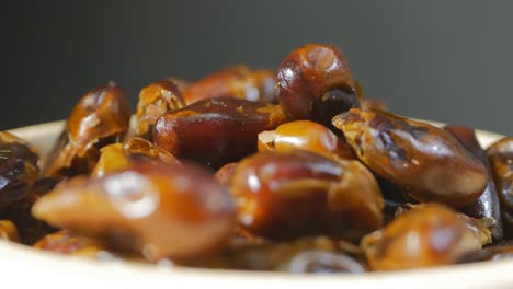 turkish sweet dates rotate in a white wood plate. the fruit shines with rays of light. dates are shot close-up on a gray background. vegetarian food concept