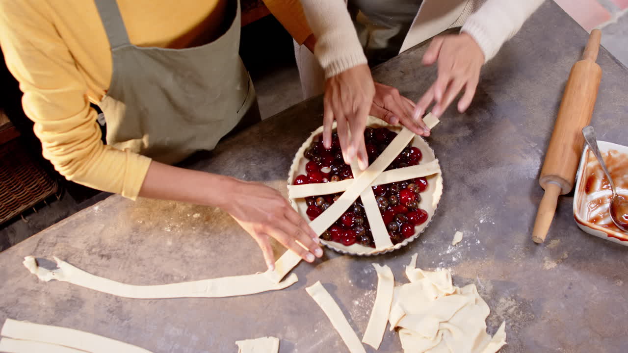 Multiracial grandma and young woman preparing cherry pie together in cozy kitchen, at home