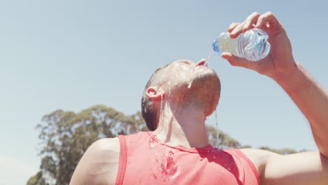 fit caucasian man pouring water over head, cooling off after exercising in sun