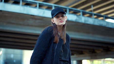 attractive woman in cap standing on city street. serious lady posing at camera