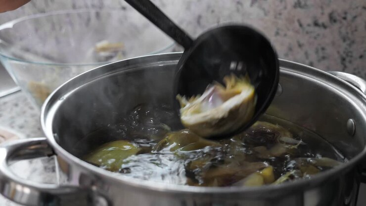 Boiling and cooking artichokes in saucepan, closeup in kitchen