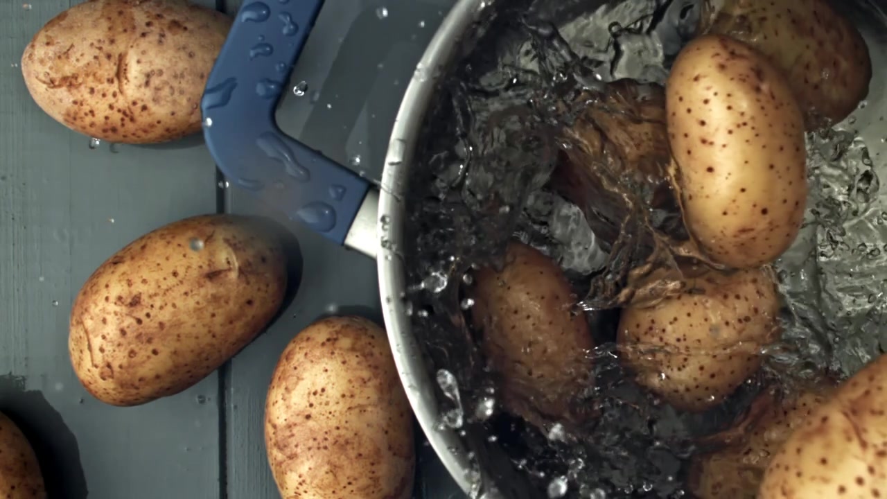 Patate fresche che cadono e schizzano in una pentola d'acqua
