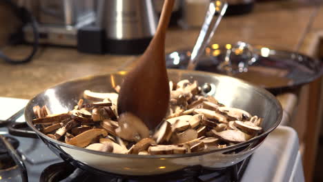 mixing raw sliced mushrooms sizzling in frying pan with wooden spoon