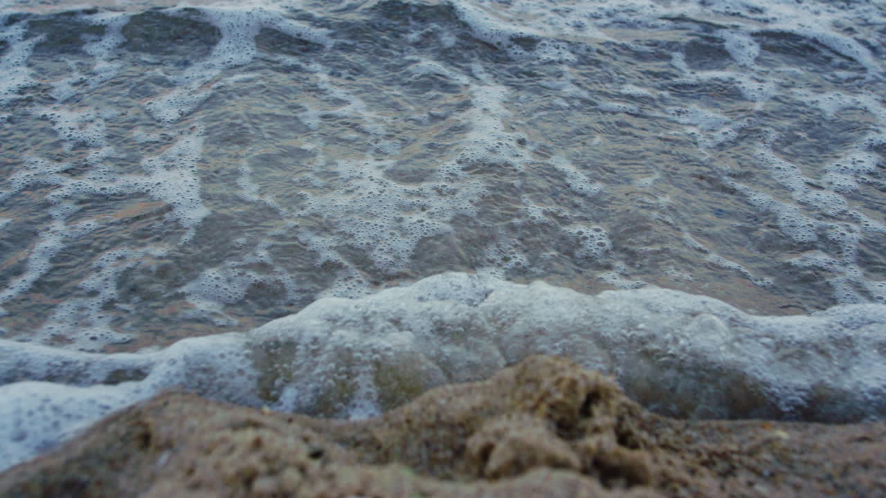 Primo piano di onde blu del mare che lavano un'impronta sulla spiaggia di sabbia. Sfondo naturale