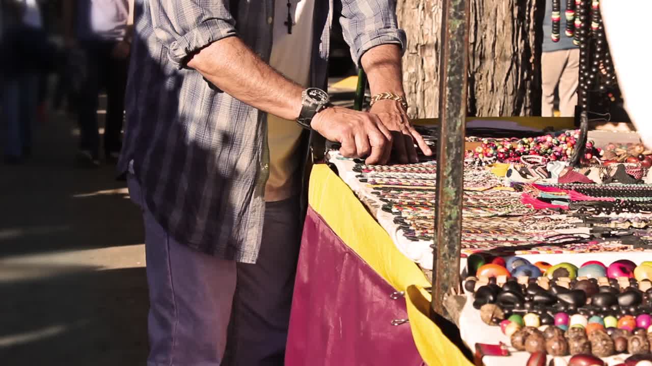 Uomo che osserva bigiotteria artigianale in una bancarella di un mercato all'aperto