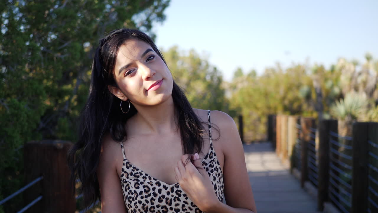 Beautiful young hispanic woman traveler walking in slow motion along a wooden path outdoors with a happy but serious stare