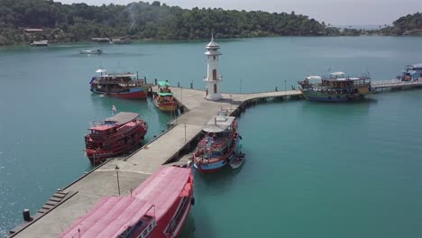 aerial view circle pan around the pier of the bang bao floating village at koh chang,thailand on a sunny day.big tourist boats boarded along side of the peir