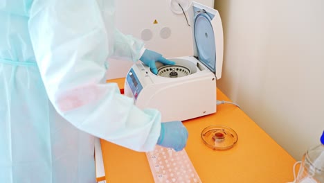 laboratory assistant near automated device for making analysis. female worker in protective uniform takes out test tubes from centrifuge in lab.