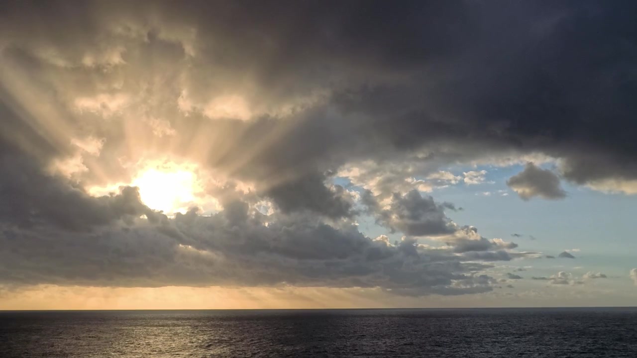 Dramatic Sunset Over Ocean with Sun Rays Through Clouds