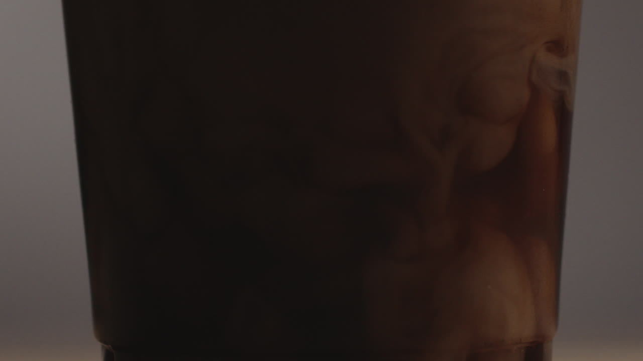 foto de producto de estudio de vidrio con café y vertiendo leche en cámara lenta sobre fondo gris