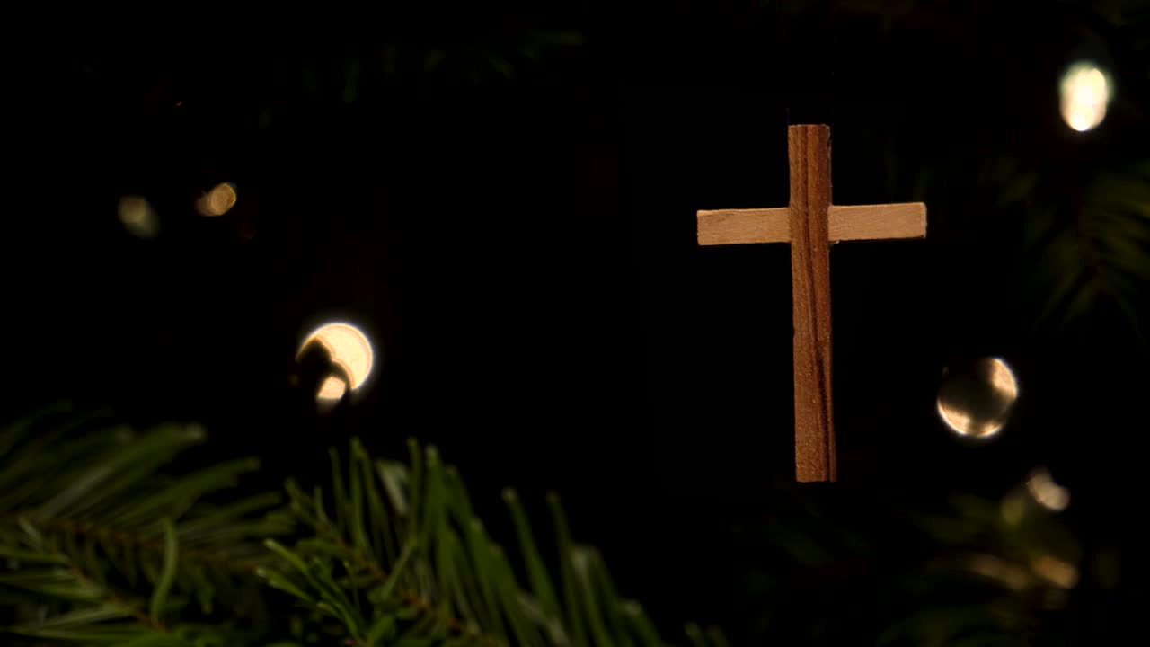 toma panorámica de un simple adorno de árbol de navidad con forma de cruz de madera colgado de un árbol