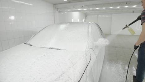 man sprinkling with foam car in white tiled room