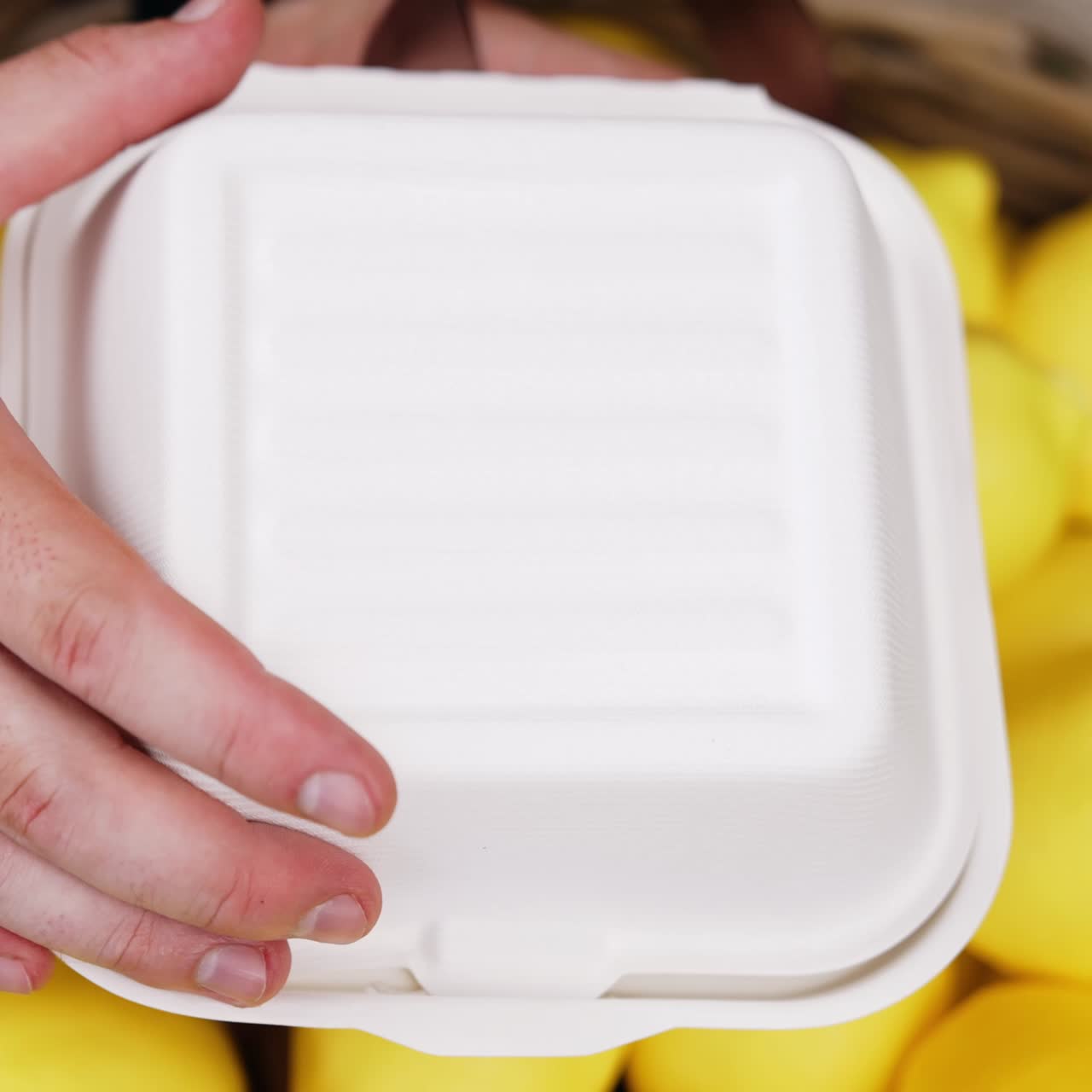 Una mano maschile apre una scatola di plastica bianca con una torta all'interno. Festeggiamento del quinto anniversario con una torta. Primo piano. Limoni sullo sfondo.