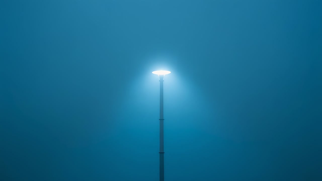 Poste de luz metálico único e brilhante emitindo luz branca fria em terreno enevoado, halo se dissipando lentamente