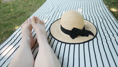 female feet and summer straw hat placed on striped mattress on the ground in shade