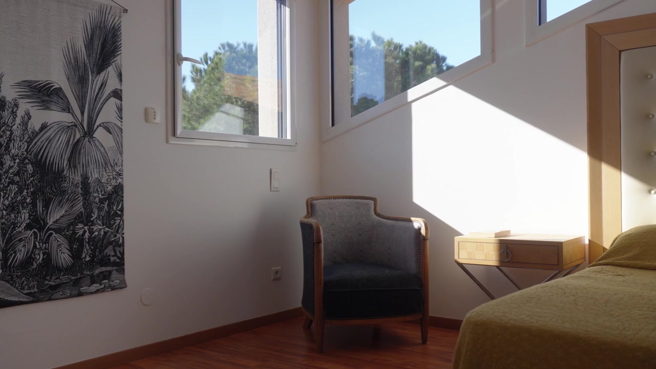 La luce del sole attraversa una camera da letto moderna con sedia, tavolino e grandi finestre.