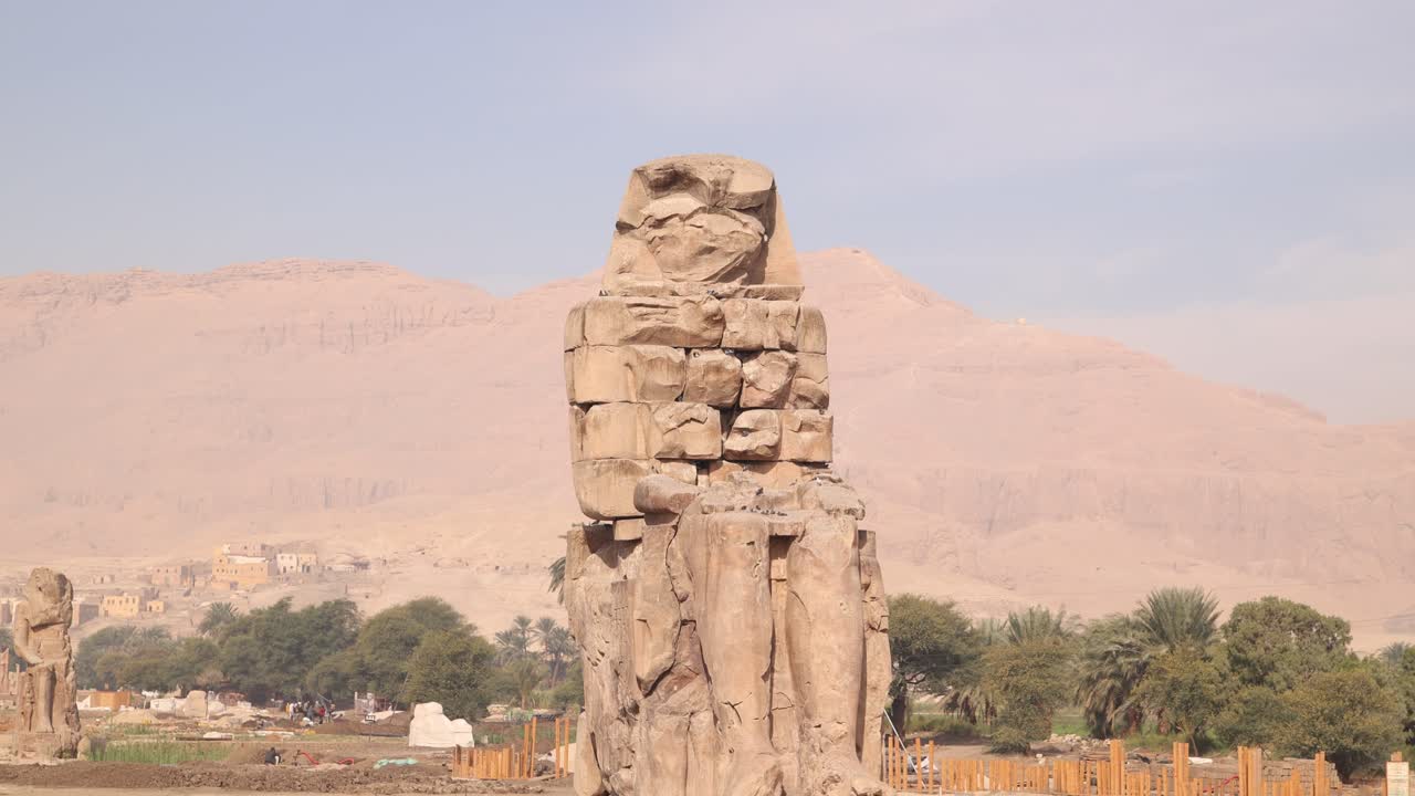 ruinas de la estatua gigante de faraón con montañas en el fondo en los colosos de memnon en luxor, egipto