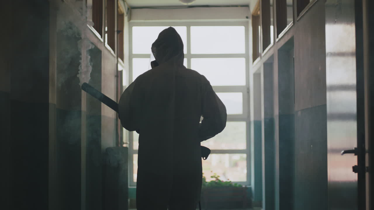 Person in hazmat suit with smoke and weapon in hallway