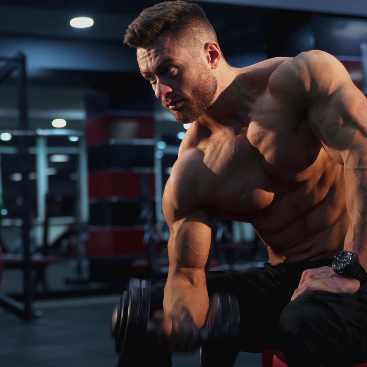 Ragazzo attraente con corpo atletico si esercita con un manubrio. Sportivo a torso nudo allena i bicipiti con pesi pesanti in palestra