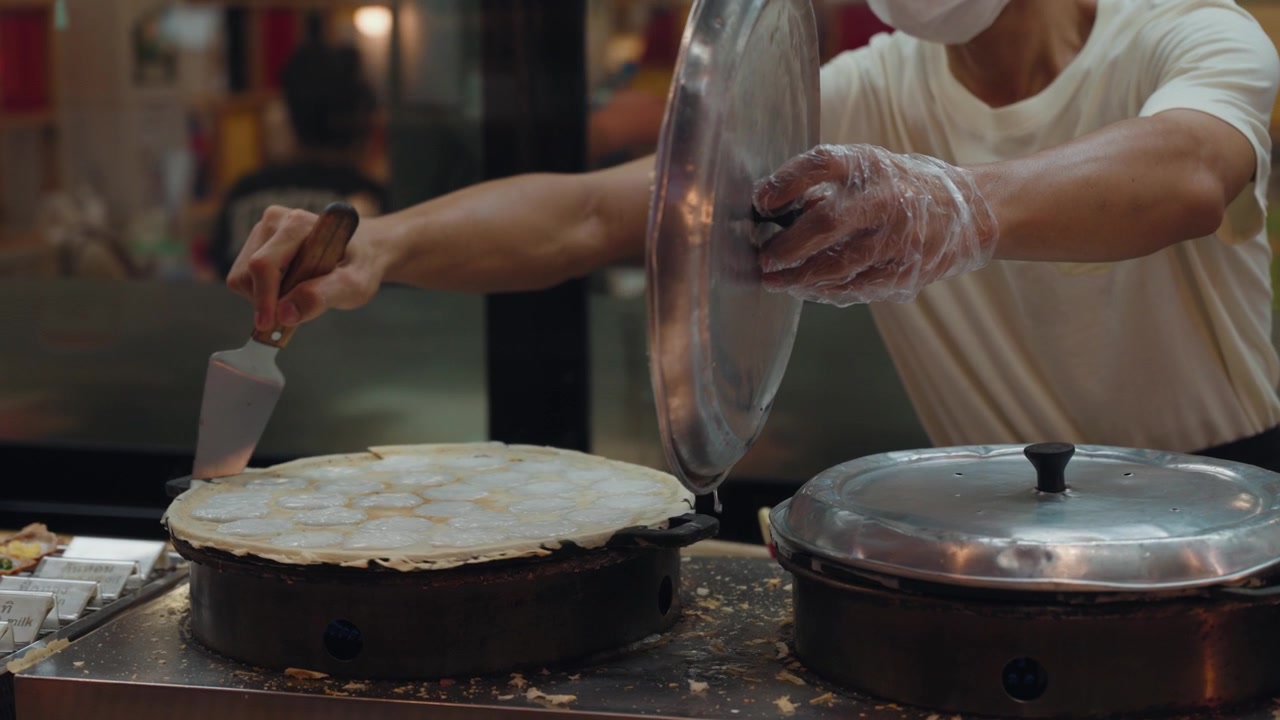 Venditore di street food che cucina crepes tradizionali su piastra rovente