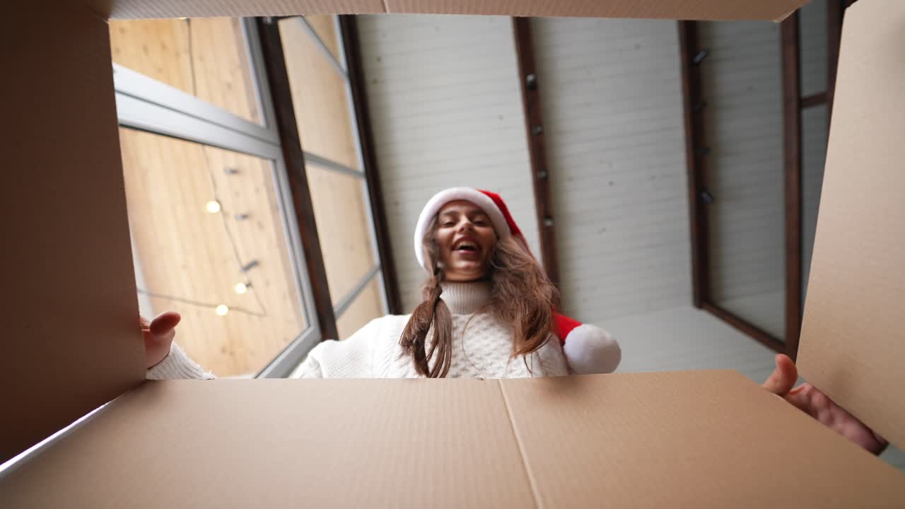 женщина с волнением открывает коробку с рождественским подарком.