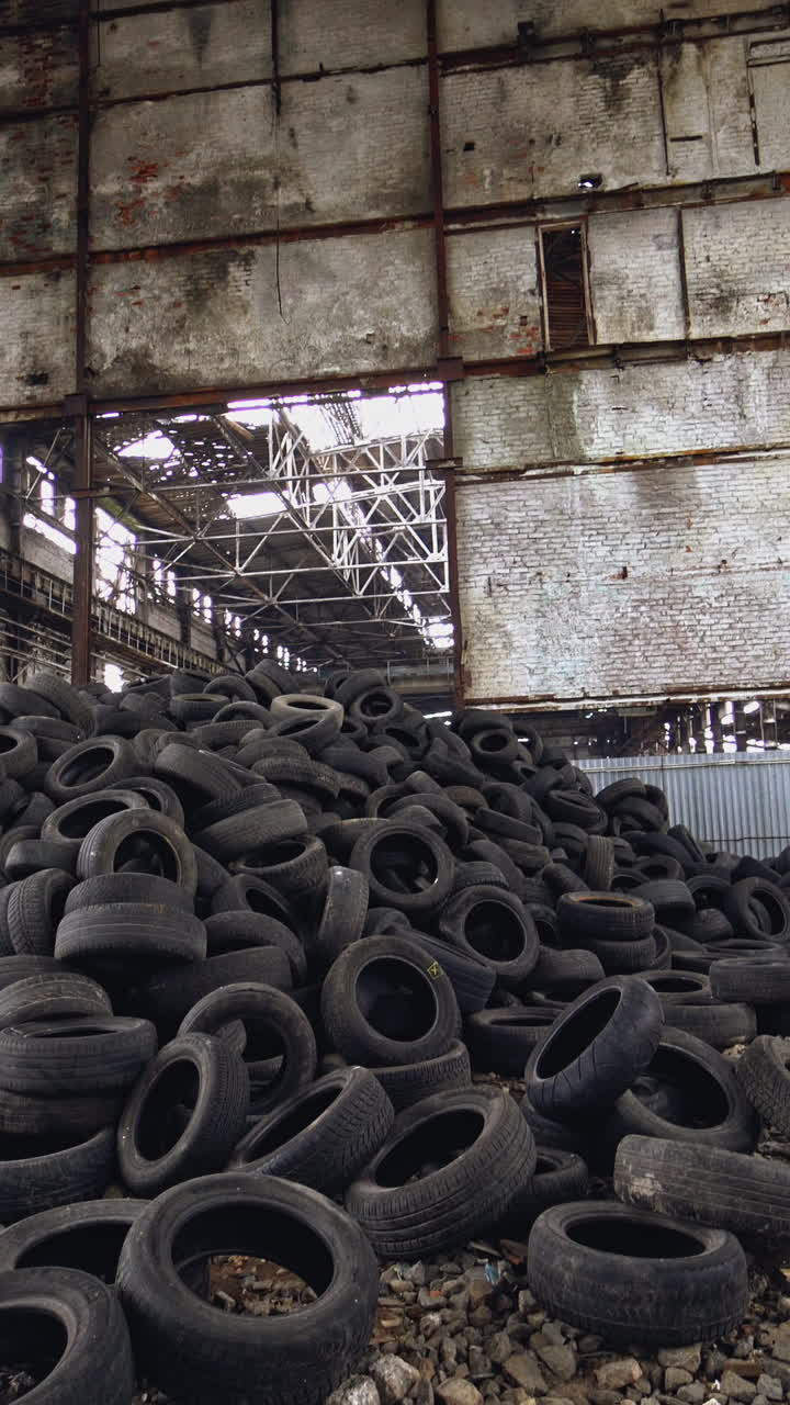 Many waste rubber tires lying on the ground inside the old factory. Big pile of used black car wheels on the empty territory. Camera moves bottom up Vertical video