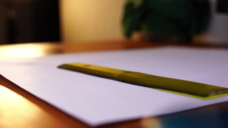 small bright ruler is placed on a sheet on a wooden writing table and off again