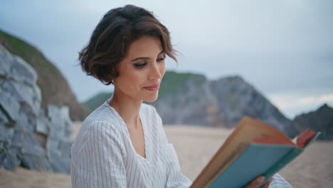 smiling model reading book on rocky seashore closeup. beautiful woman outdoors