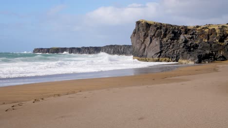 Serena-Playa-Islandesa-Con-Acantilados-Escarpados-Y-Olas-Rompiendo-En-La-Orilla,-Huellas-En-La-Arena-Insinúan-A-Los-Visitantes-Recientes.