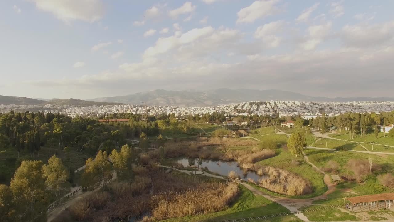 AERIAL city view with a amazing green park above  trees and small lake city building at background sunny day with few clouds in sky