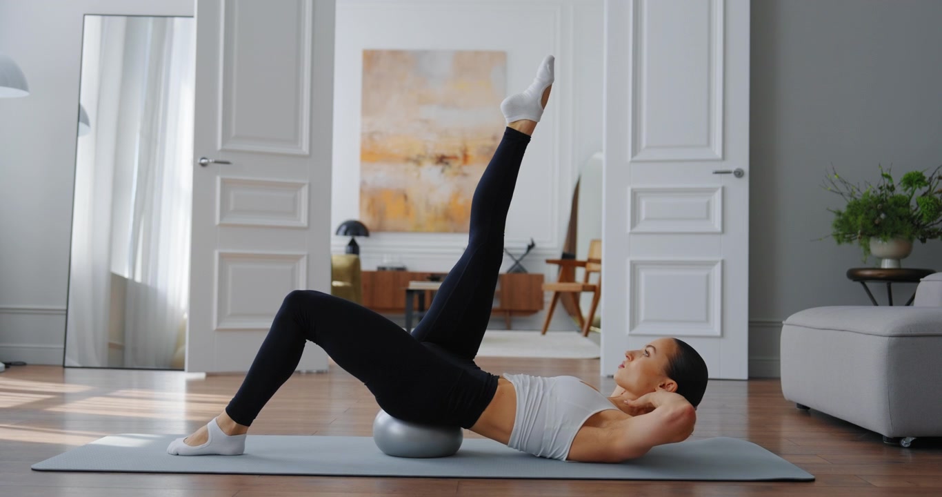 Giovane donna esegue sollevamenti delle gambe Pilates sulla fitball a casa