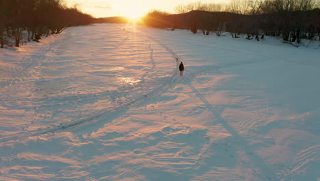 a person plays fetch with a dog on a snow covered frozen river during a beautiful winter sunset