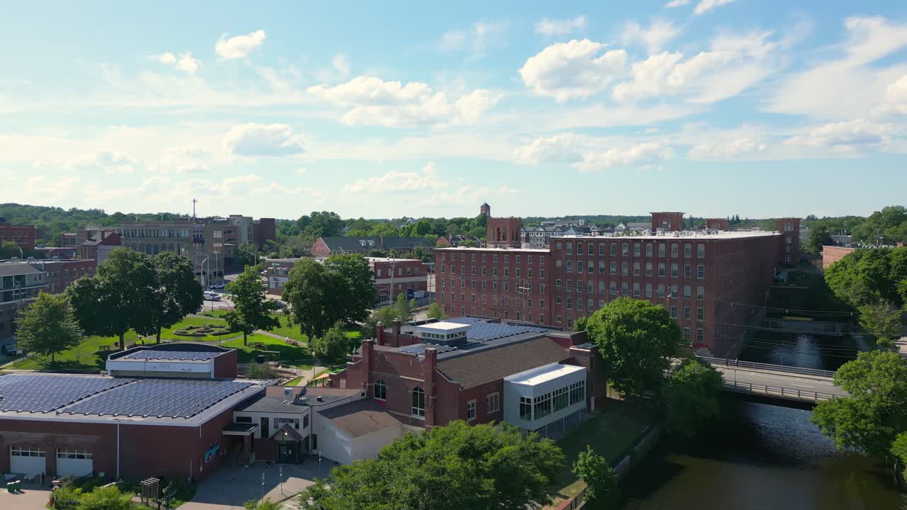 Drohnenaufnahme, die langsam über einen Fluss auf eine alte Ziegelmühle in Dover, NH, USA, zufliegt. Sie steigt dann auf, um das Stadtzentrum zu zeigen, während sie nach unten neigt und kreist.