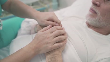 detalle de las manos de una enfermera agarrando y consolando las manos de un paciente enfermo en la cama del hospital