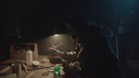 a bombmaker assembles a bomb in his workshop at night