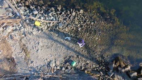 aerial zoom out of woman removing plastic waste from shore of norway fjord