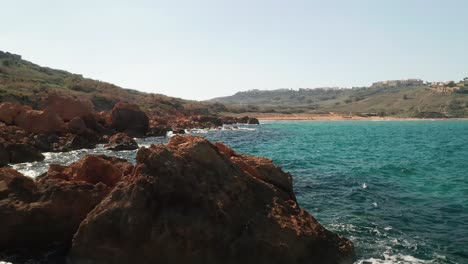 Aerial-dolly-shot-of-a-seashore-with-beautiful-red-coloured-rocks-and-turquoise-waters-of-the-Mediterranean-Sea,-Ramla-Beach-on-the-island-of-Gozo,-Malta