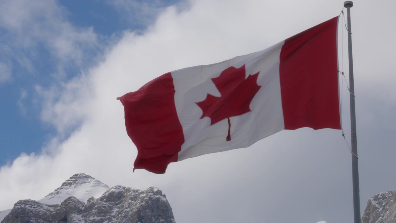 Bandiera canadese che sventola al vento contro il cielo blu e le montagne innevate
