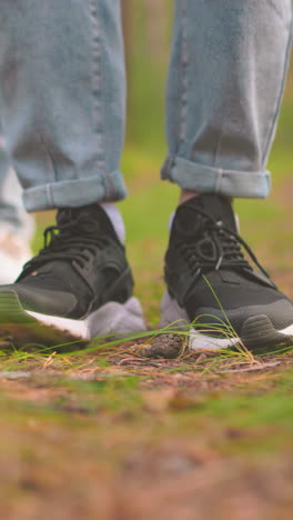 primer plano de dos individuos de pie en el sendero del bosque en vaqueros azules, uno en zapatillas negras y otro en zapatillas blancas, persona en zapatillas negras golpea la pierna en el suelo