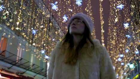 a beautiful girl walks gracefully under stunning christmas lights, admiring the festive atmosphere on a chilly evening in moscow. the streets twinkle with holiday cheer.